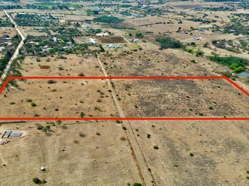 An aerial view of a large, flat, vacant residential plot of land with clear boundary markings, situated in a rural or semi-rural area.