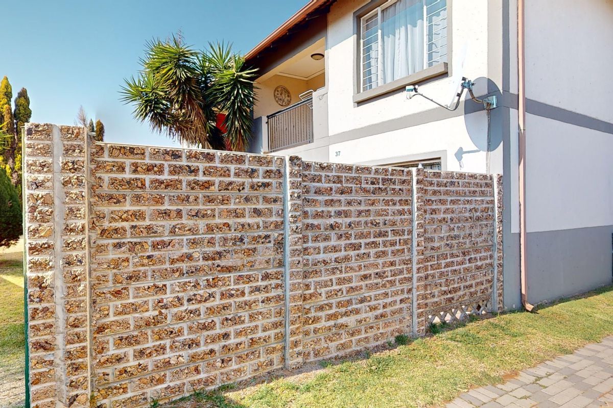 Rear view of the apartment building featuring a textured precast concrete boundary wall, a small balcony, and a paved walkway.