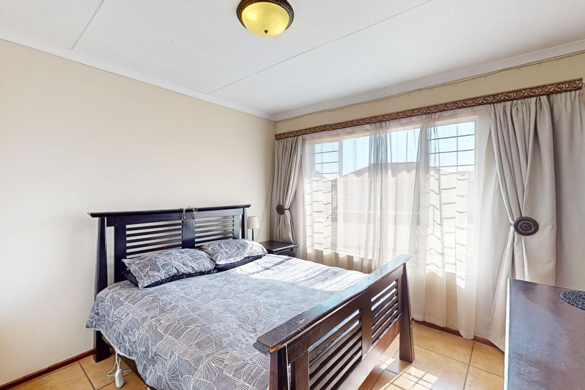A functional bedroom featuring tiled flooring, a central ceiling light, and a window fitted with security bars.
