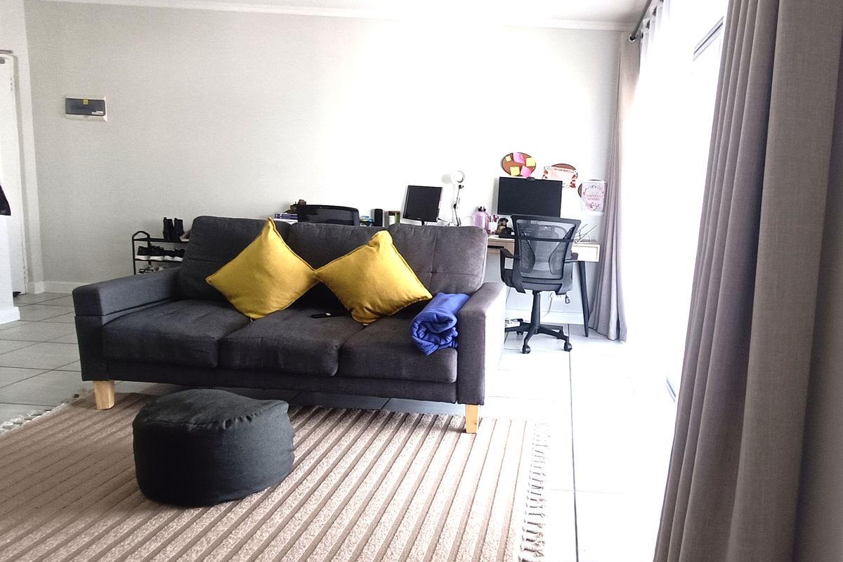 A living room area featuring tiled flooring and a large sliding glass door with curtains, providing access to natural light.