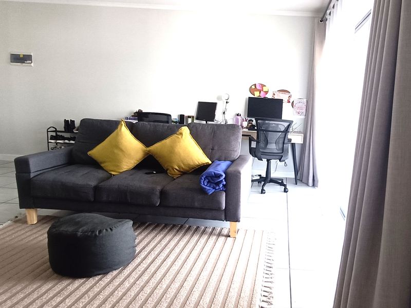 A living room area featuring tiled flooring and a large sliding glass door with curtains, providing access to natural light.