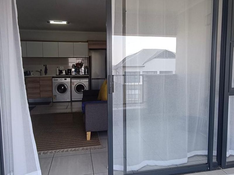 View from a balcony into an open-plan living and kitchen area featuring modern cabinetry, tiled floors, and integrated laundry appliances.
