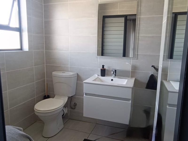 A modern, clean bathroom featuring a wall-mounted vanity, ceramic basin, chrome fixtures, and neutral wall tiling.
