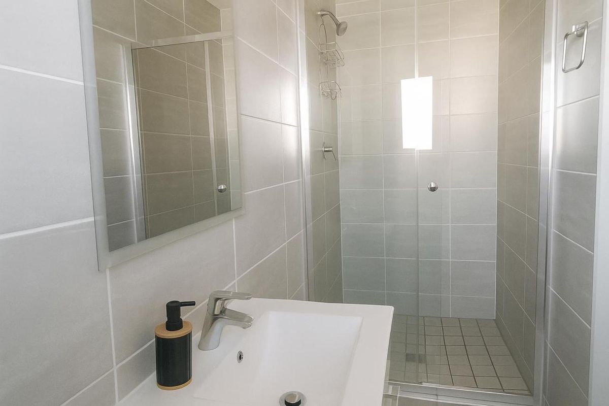 Modern bathroom featuring a glass-enclosed shower, wall-mounted mirror, and a clean vanity basin with contemporary tiling.