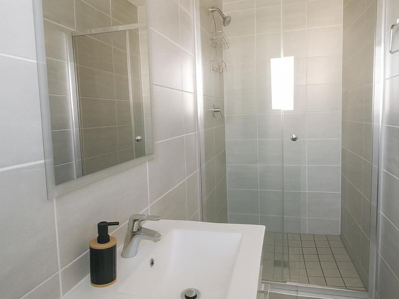 Modern bathroom featuring a glass-enclosed shower, wall-mounted mirror, and a clean vanity basin with contemporary tiling.