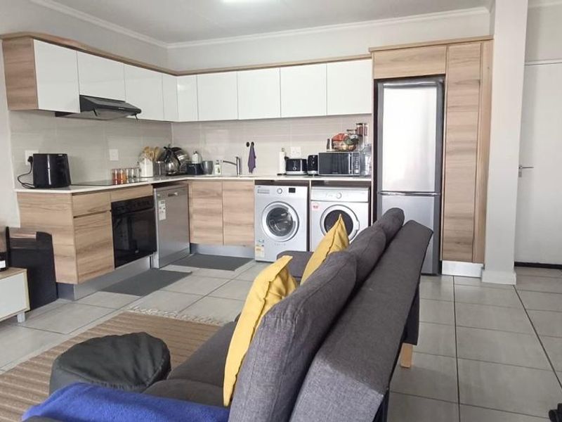 Open-plan living area featuring a modern kitchen with built-in cabinetry, integrated appliances, and tiled flooring throughout.