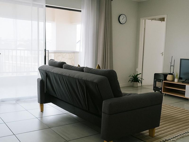 A bright living room featuring neutral tiled flooring and a large sliding glass door providing access to an outdoor balcony area.