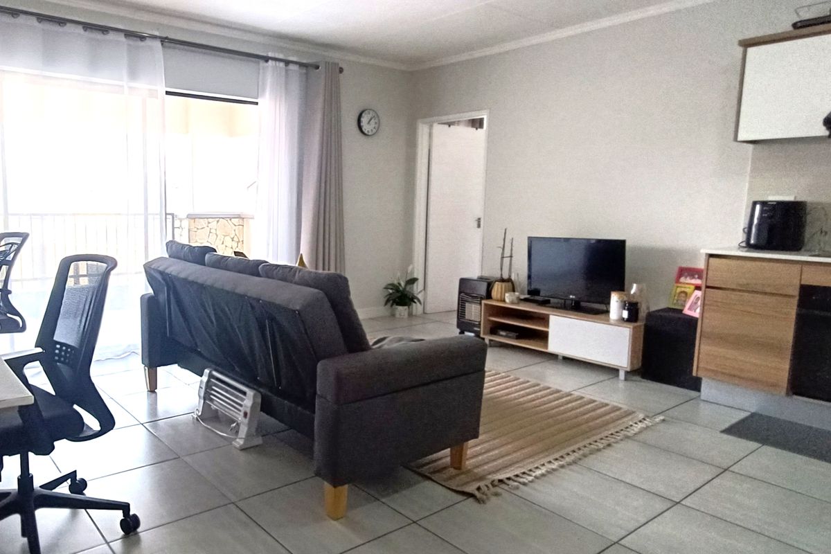Open-plan living area featuring tiled flooring, integrated kitchen cabinetry with built-in oven and extractor fan, and direct access to a balcony.