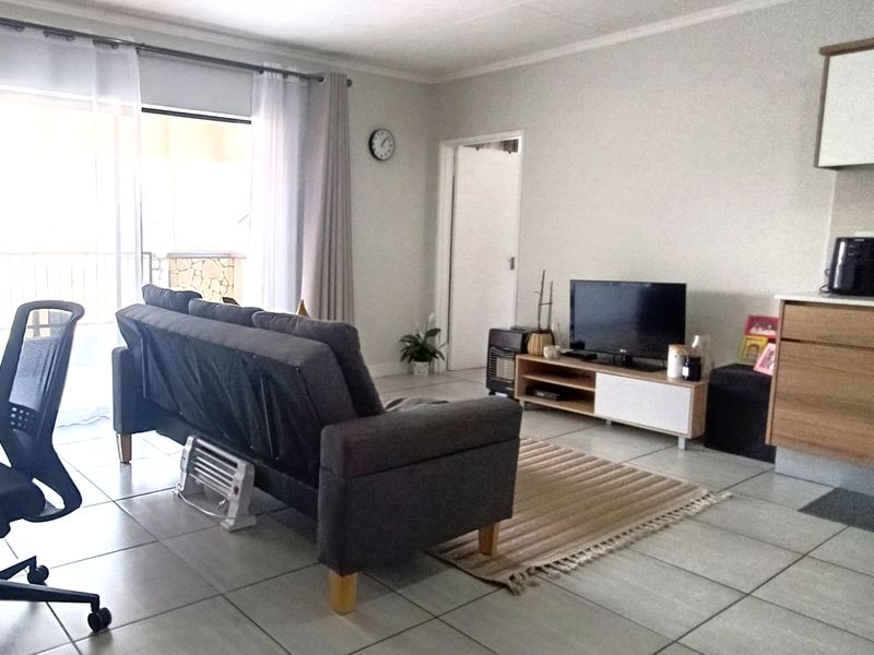 Open-plan living area featuring tiled flooring, integrated kitchen cabinetry with built-in oven and extractor fan, and direct access to a balcony.