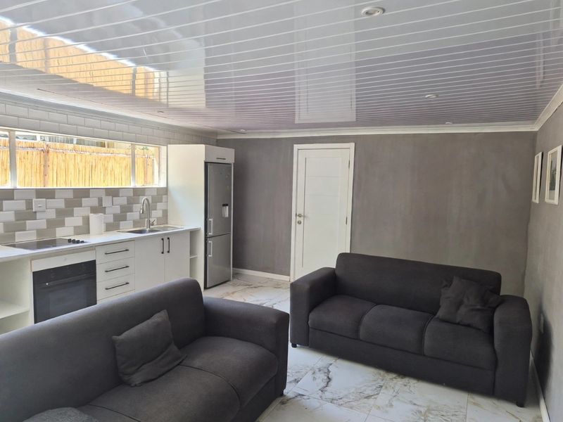 Open-plan living area featuring a modern kitchen with built-in cabinetry, integrated appliances, marble-look flooring, and a glossy panelled ceiling.