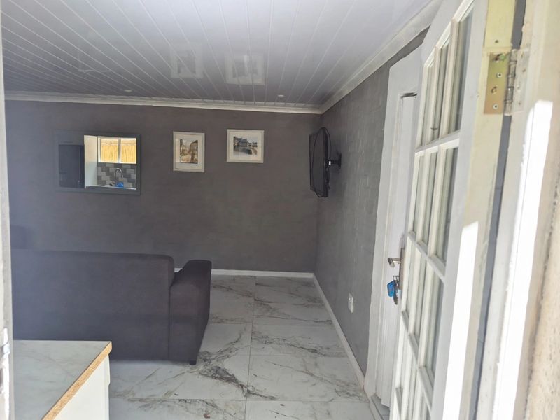 A living room featuring marble-look floor tiles, a tongue and groove ceiling, and a convenient pass-through window connecting to the kitchen area.