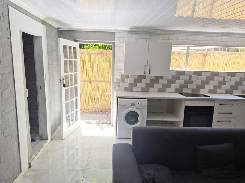 Open plan living area featuring a modern kitchen with subway tile backsplash, built-in oven, hob, and direct access to an outdoor patio area.