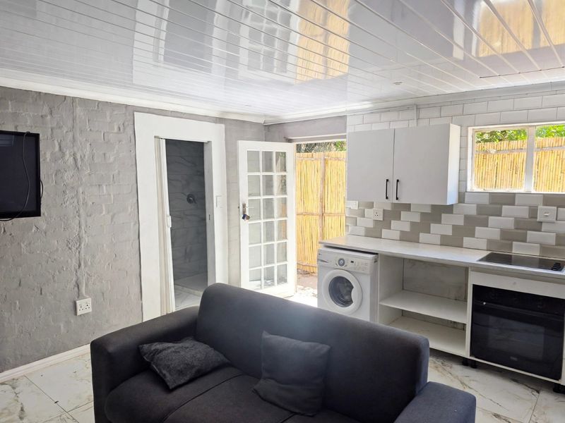 Open-plan living area featuring a compact kitchen with built-in oven, hob, and cabinetry, leading directly to an outdoor space.