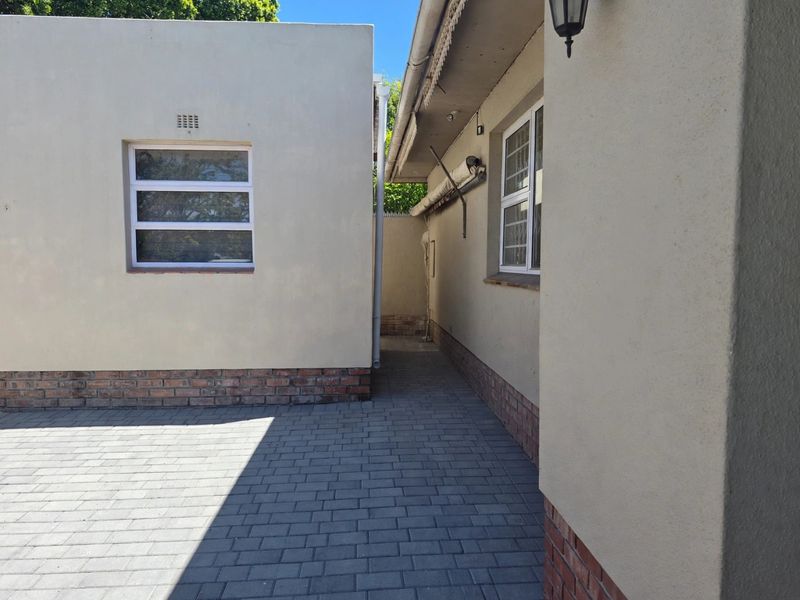 A clean, paved rear courtyard area featuring plastered walls with brick plinth detailing and aluminium window frames.