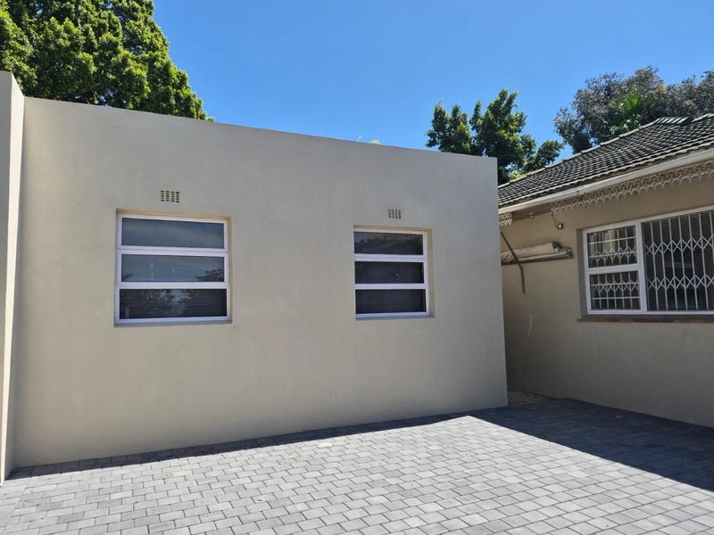 A clean rear exterior view featuring a paved courtyard area, modern aluminium windows with security bars, and a well-maintained building facade.