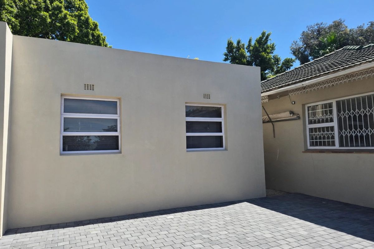 A clean rear exterior view featuring a paved courtyard area, modern aluminium windows with security bars, and a well-maintained building facade.
