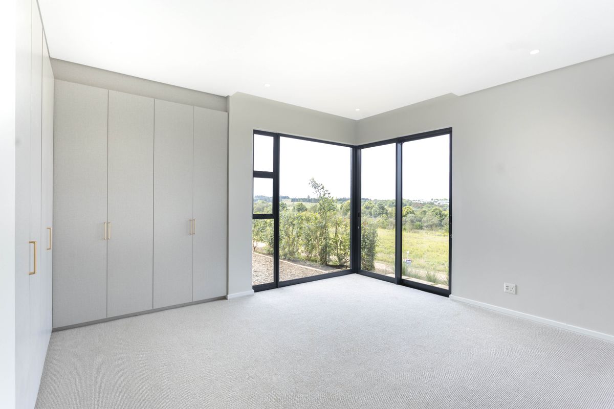 A bright, modern bedroom featuring neutral carpeting, extensive built-in cabinetry, and large corner windows offering scenic landscape views.