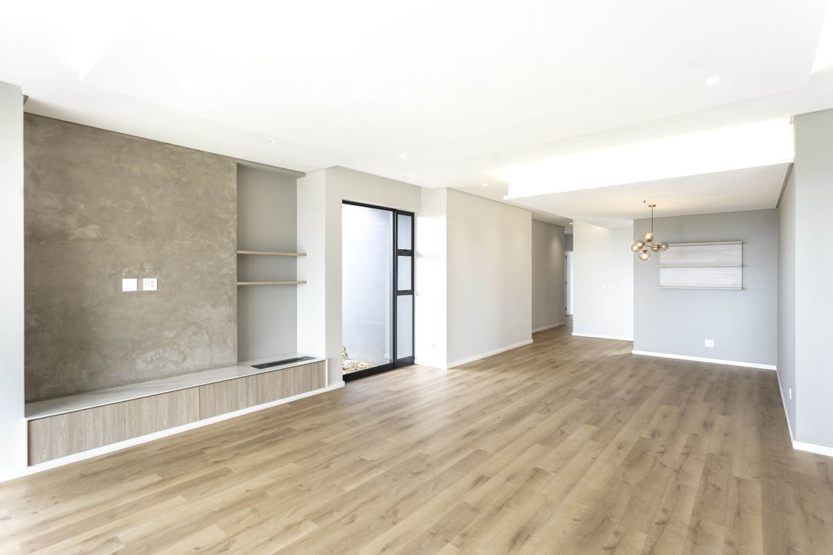Spacious, modern living area featuring light wood-look flooring, a textured feature wall with built-in cabinetry, and elegant recessed cove lighting.