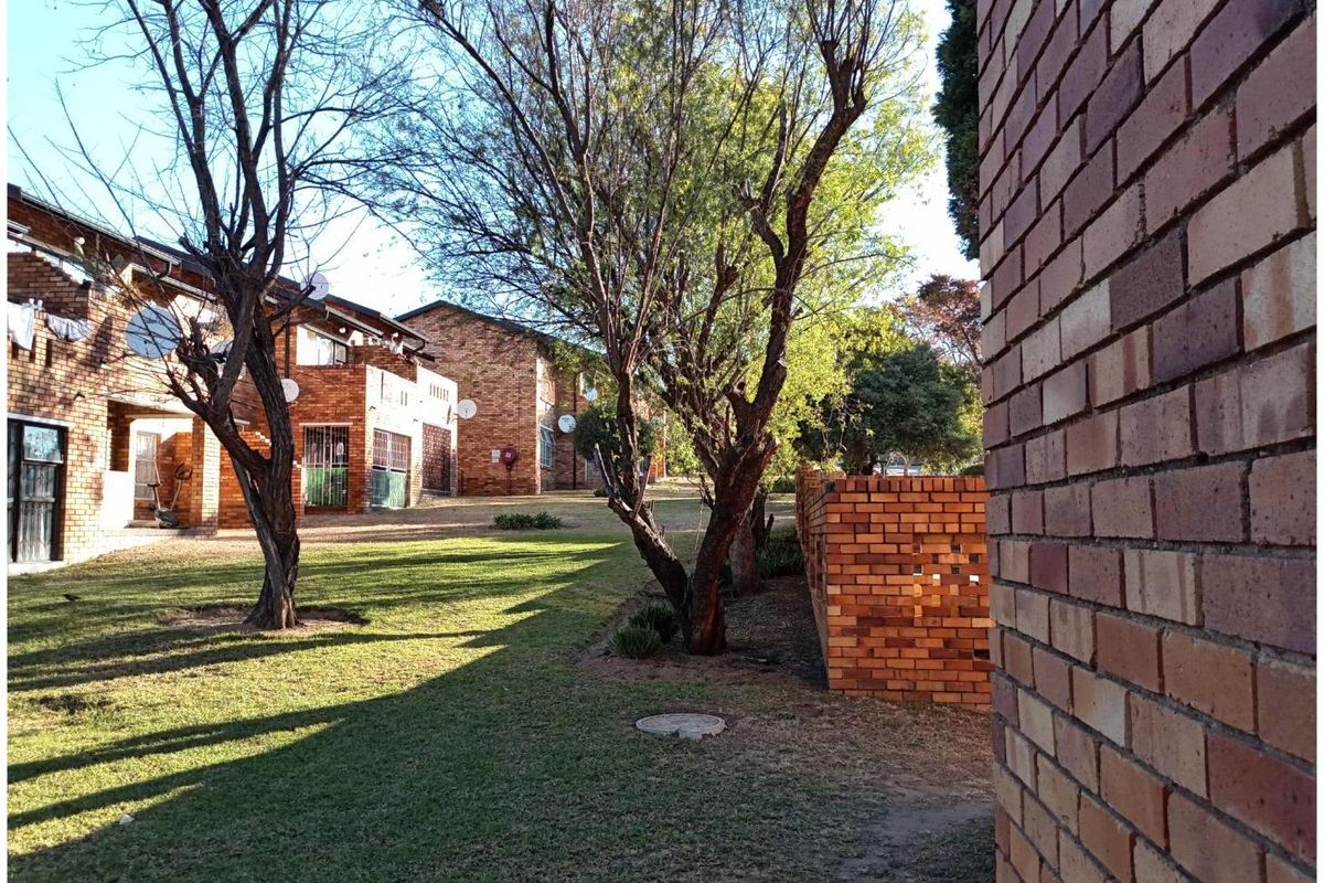 A view of the communal garden area between apartment blocks, featuring established trees, brick boundary walls, and well-maintained lawn space.