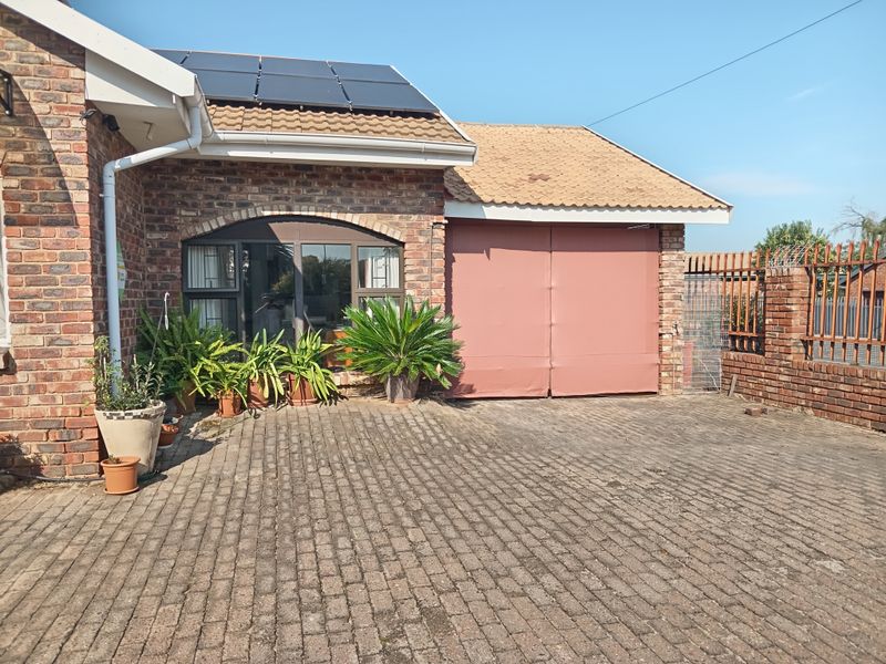 Front exterior view of a brick townhouse featuring a paved driveway, solar panels on the roof, and a secure boundary wall.