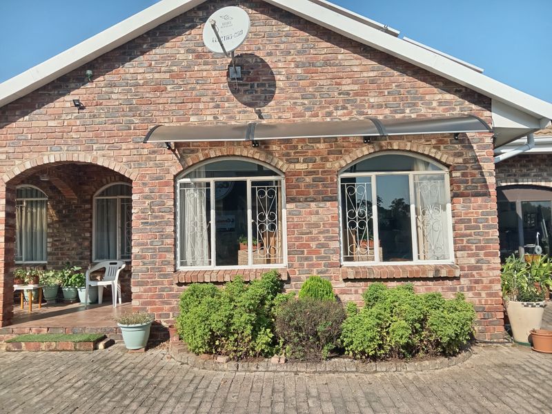 Front elevation of a face brick townhouse featuring arched windows with security bars, a covered porch area, and a paved driveway.