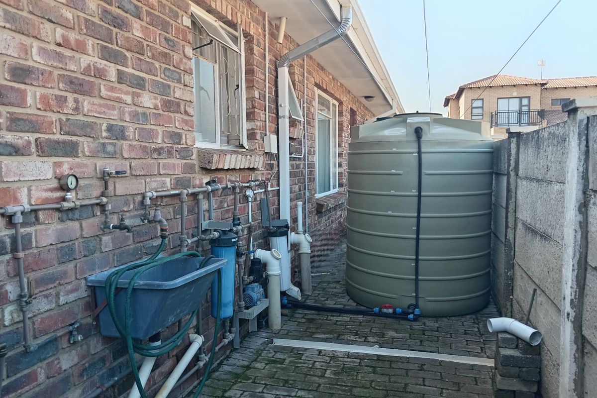 Rear exterior area featuring a large water storage tank, integrated water filtration system, utility sink, and exposed plumbing against a brick townhouse wall.