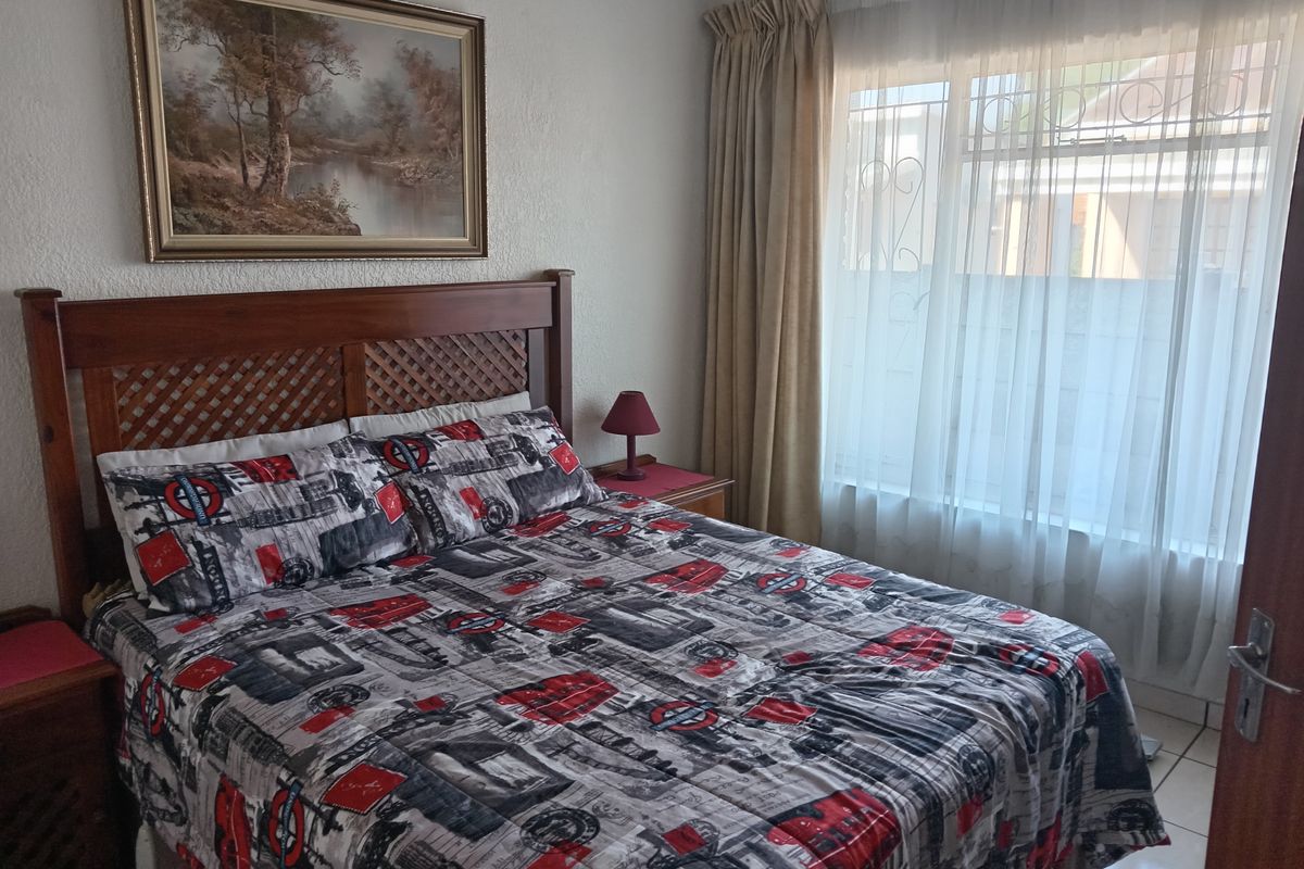 A well-lit bedroom featuring tiled flooring and a large window with curtain rails, providing a functional and comfortable living space.