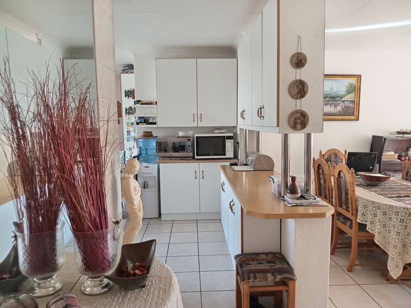 Open plan kitchen area featuring white cabinetry, laminate countertops, and ceramic floor tiles, seamlessly connecting to the adjacent dining space.