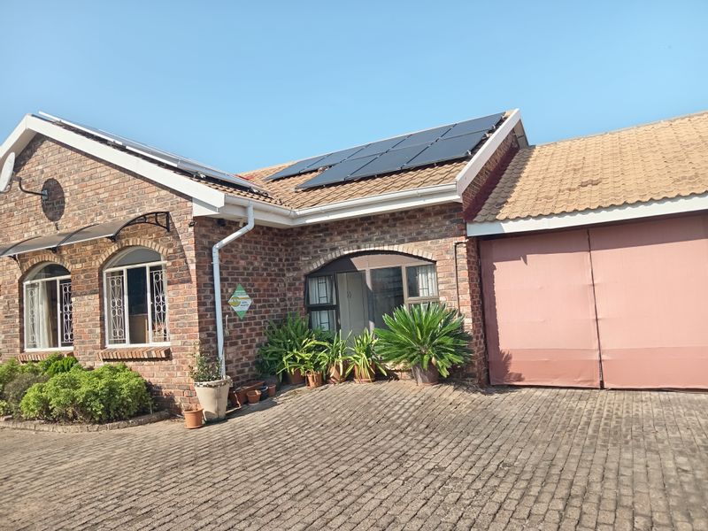 Front elevation of a face brick townhouse featuring a paved driveway, solar panels on the roof, and arched window detailing.