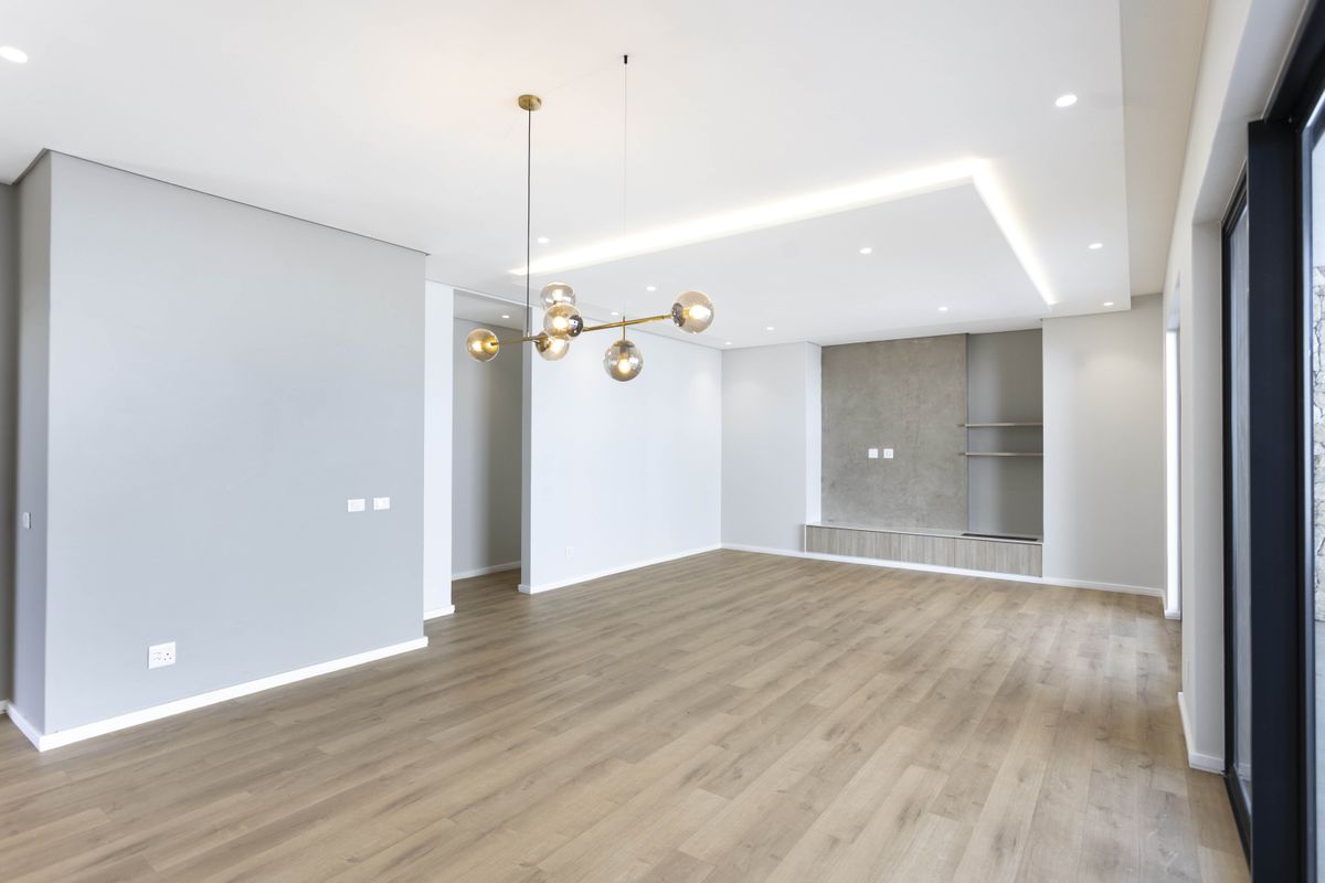 A bright, modern living room featuring light wood-look flooring, recessed ceiling lighting, and a custom built-in media unit with a feature wall.