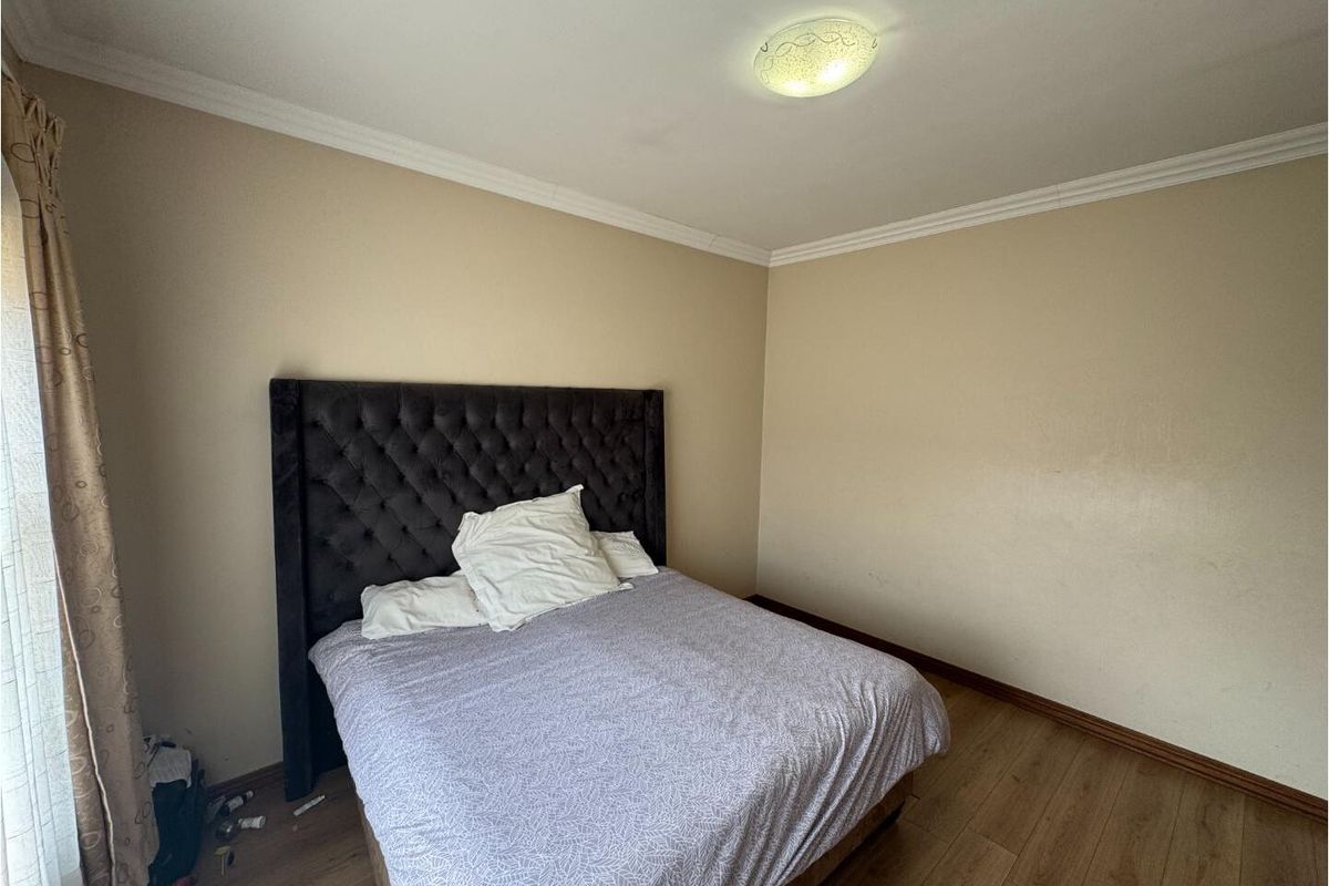 A standard bedroom featuring laminate flooring, neutral wall tones, and decorative ceiling cornicing, providing a functional and blank canvas for personalization.