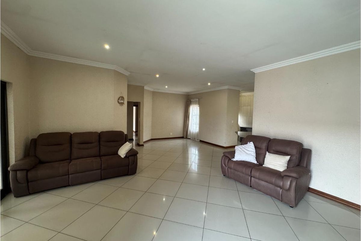Spacious open-plan living area featuring neutral tiled flooring, recessed downlighting, and coved cornicing throughout.