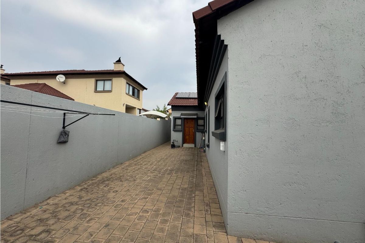 A side exterior walkway featuring paved flooring, a high boundary wall, and access to a rear entrance door.