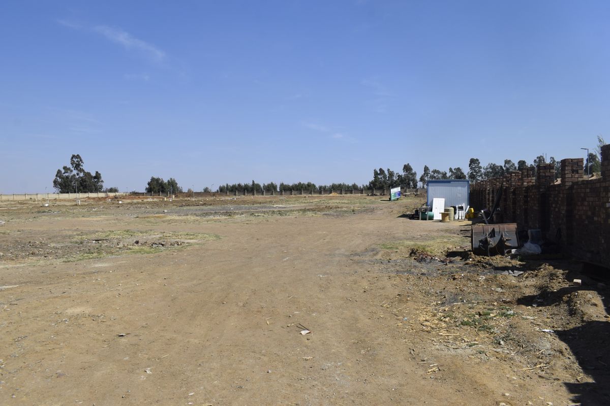 A vacant residential plot featuring cleared land and a brick boundary wall, ready for development.