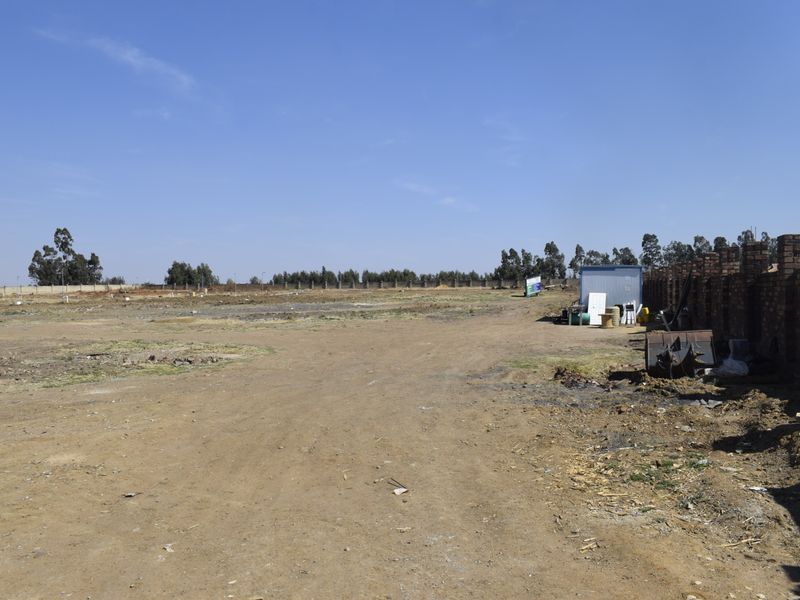 A vacant residential plot featuring cleared land and a brick boundary wall, ready for development.
