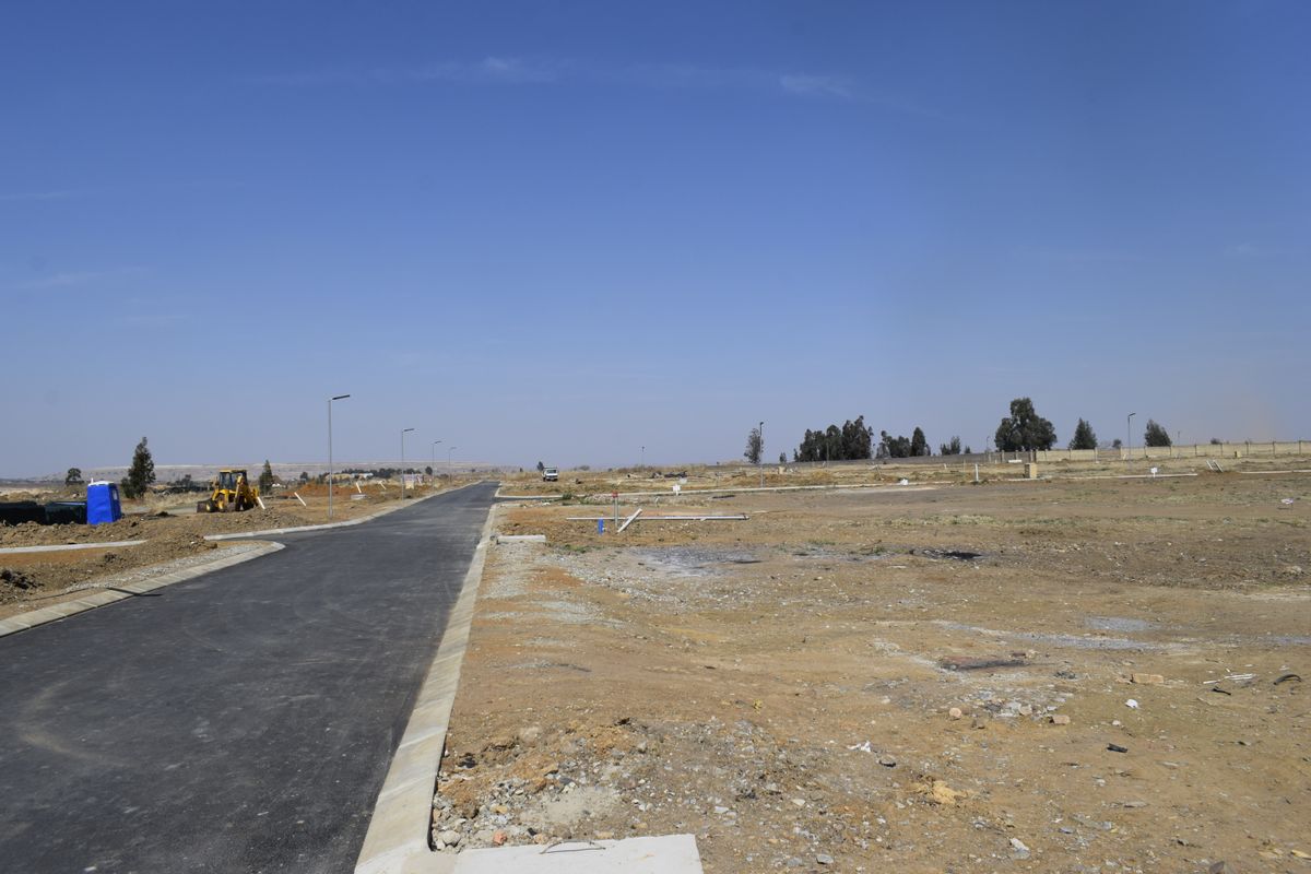 A view of a newly developed residential street with paved roads, concrete curbing, and visible utility connections on a vacant land plot.
