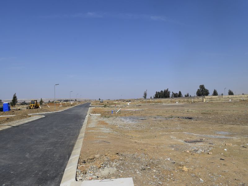 A view of a newly developed residential street with paved roads, concrete curbing, and visible utility connections on a vacant land plot.