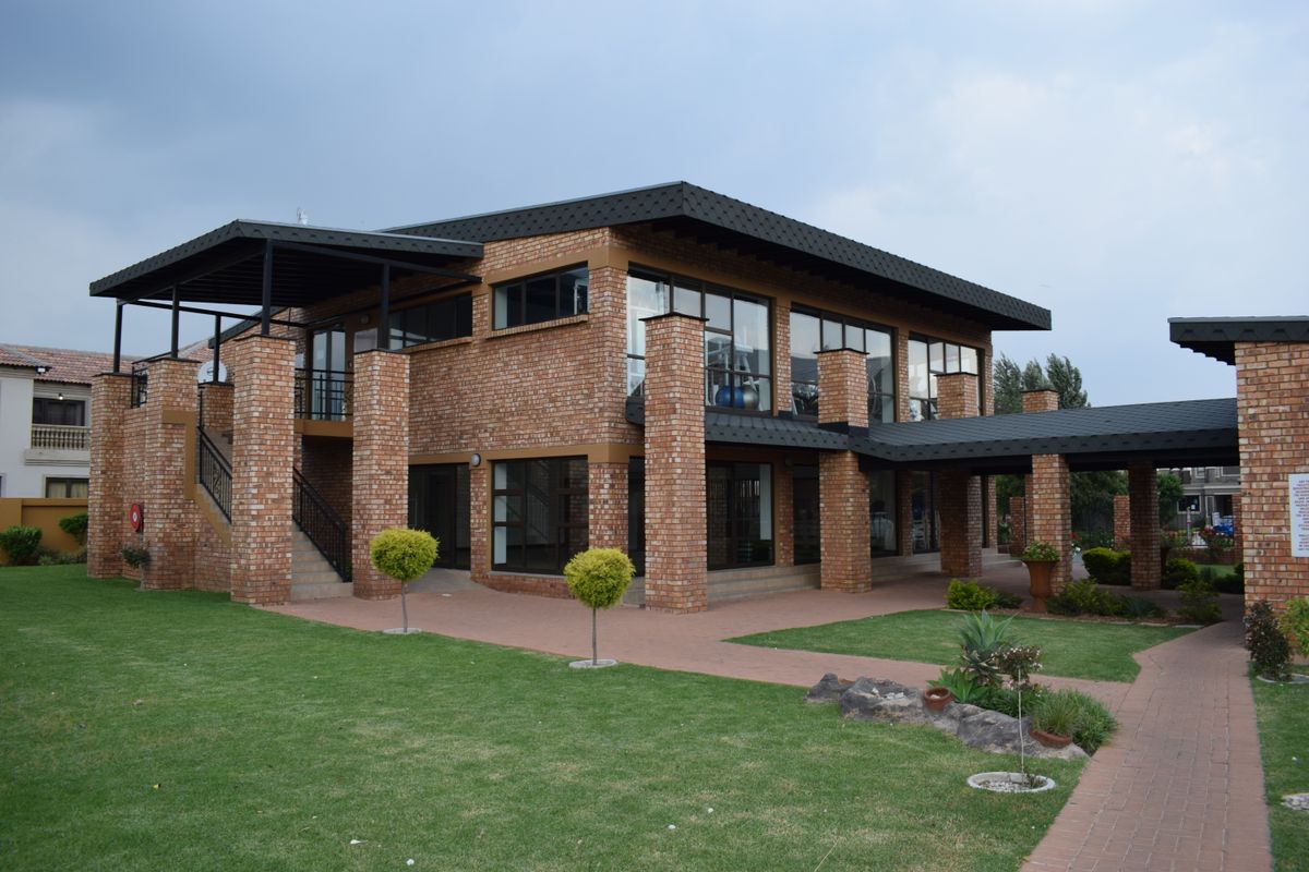 A well-maintained double-story face brick building featuring a covered patio, external staircase, and landscaped garden area.