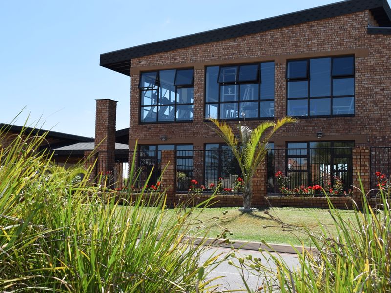A well-maintained two-story face brick building featuring large aluminium-framed windows and a landscaped garden frontage.