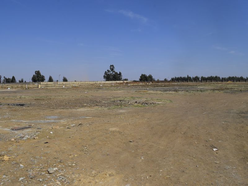 A wide-angle view of a vacant residential plot featuring cleared land and a perimeter wall, ready for development.