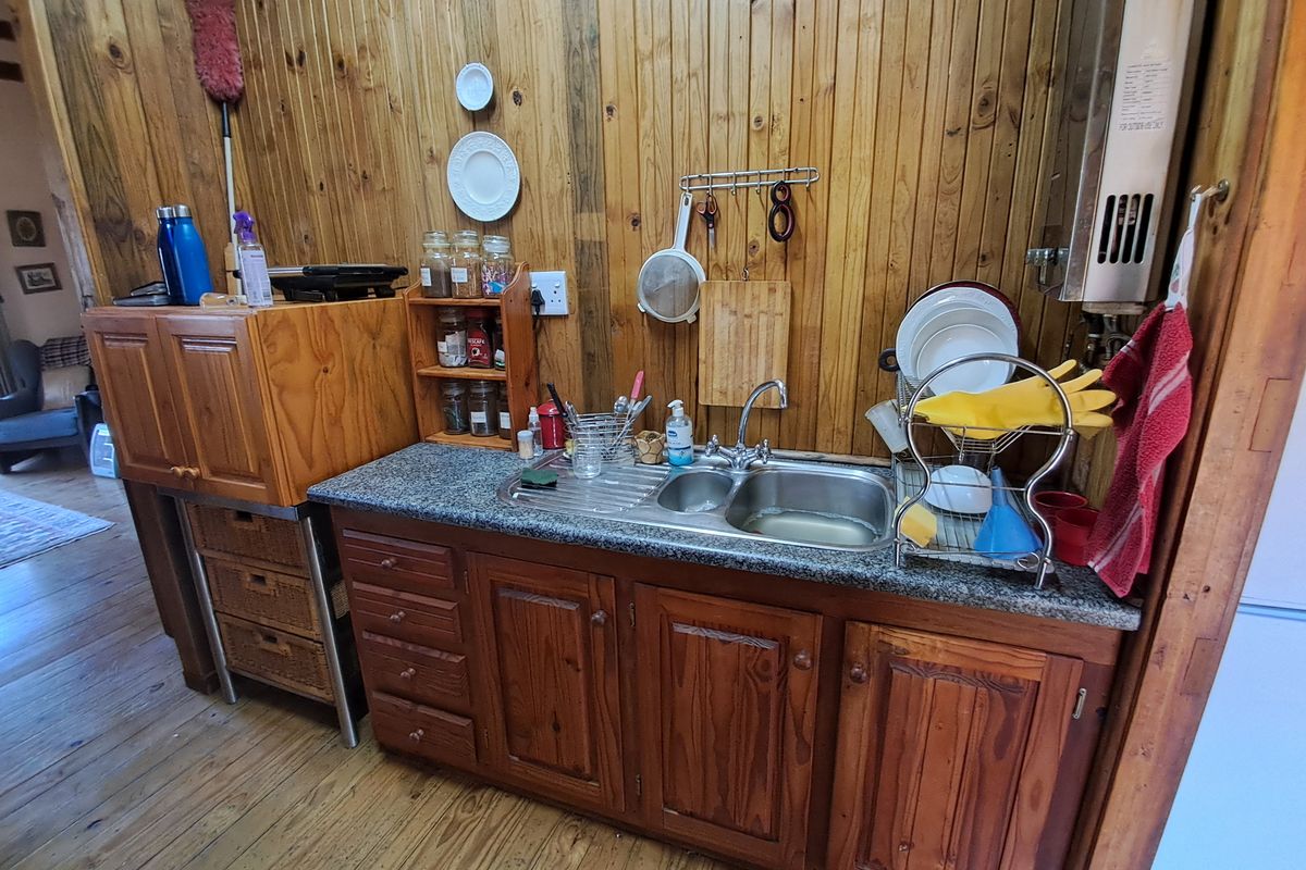 A compact kitchen area featuring timber wall paneling, granite-look laminate countertops, a stainless steel double sink, and traditional wooden cabinetry.