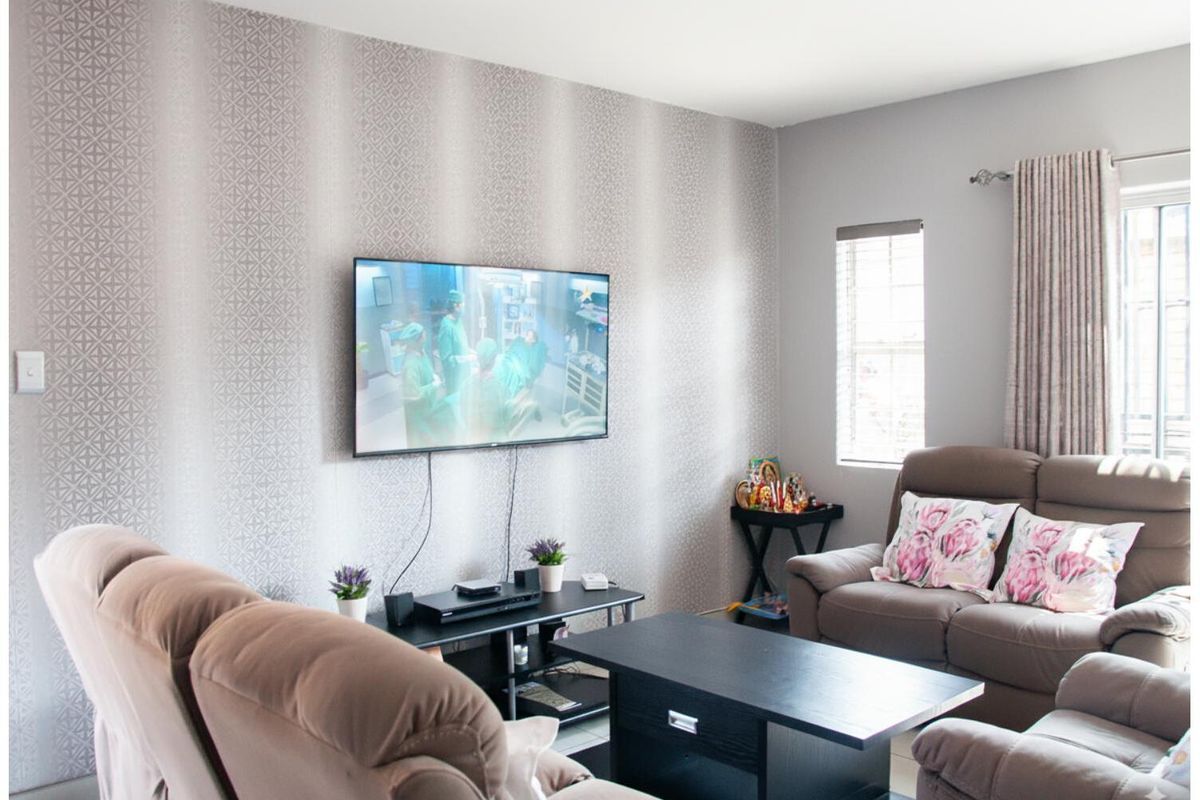 A comfortable living room featuring a patterned accent wall, neutral wall finishes, and a window with fitted curtain tracks.