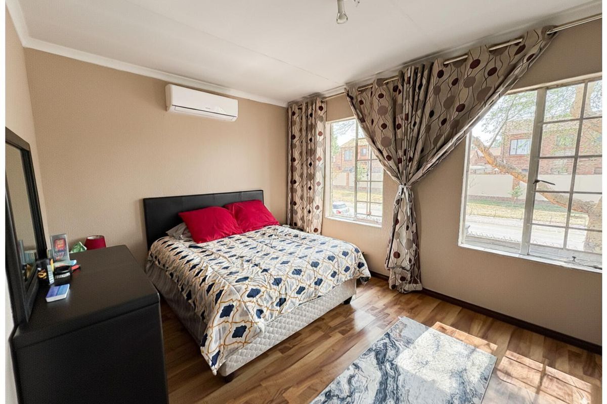 A well-lit bedroom featuring wood-look flooring, large windows, and a wall-mounted air conditioning unit.