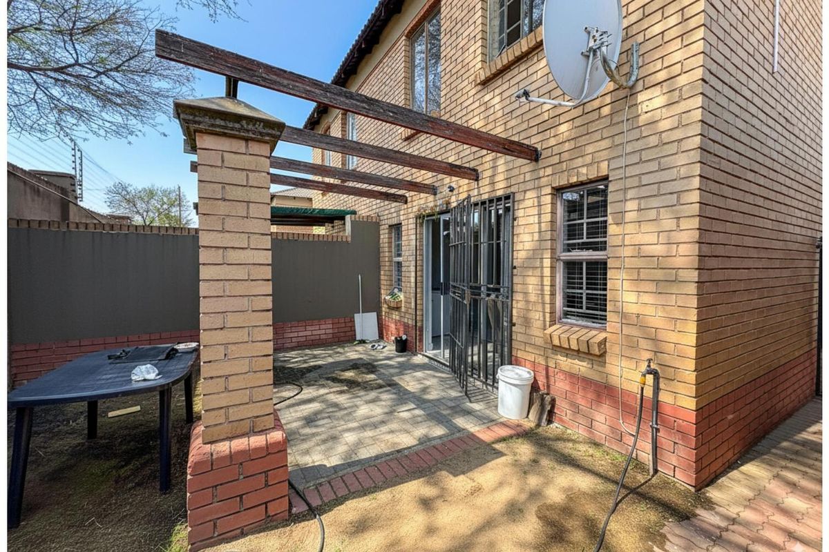 Rear exterior view of the townhouse featuring a paved patio area with a timber pergola structure and secure metal security gate access.