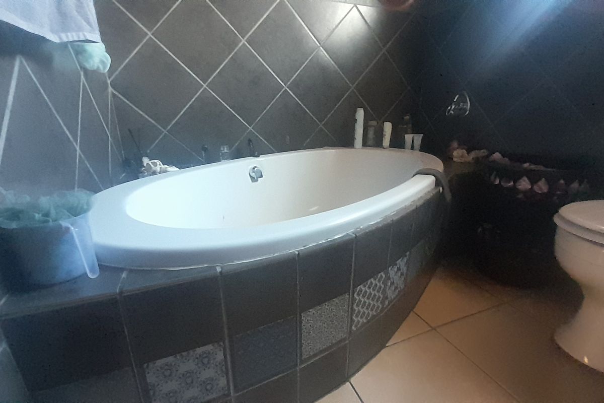 A bathroom featuring a built-in bathtub with dark tiled surround and a standard toilet, requiring cosmetic updates to improve the overall aesthetic.