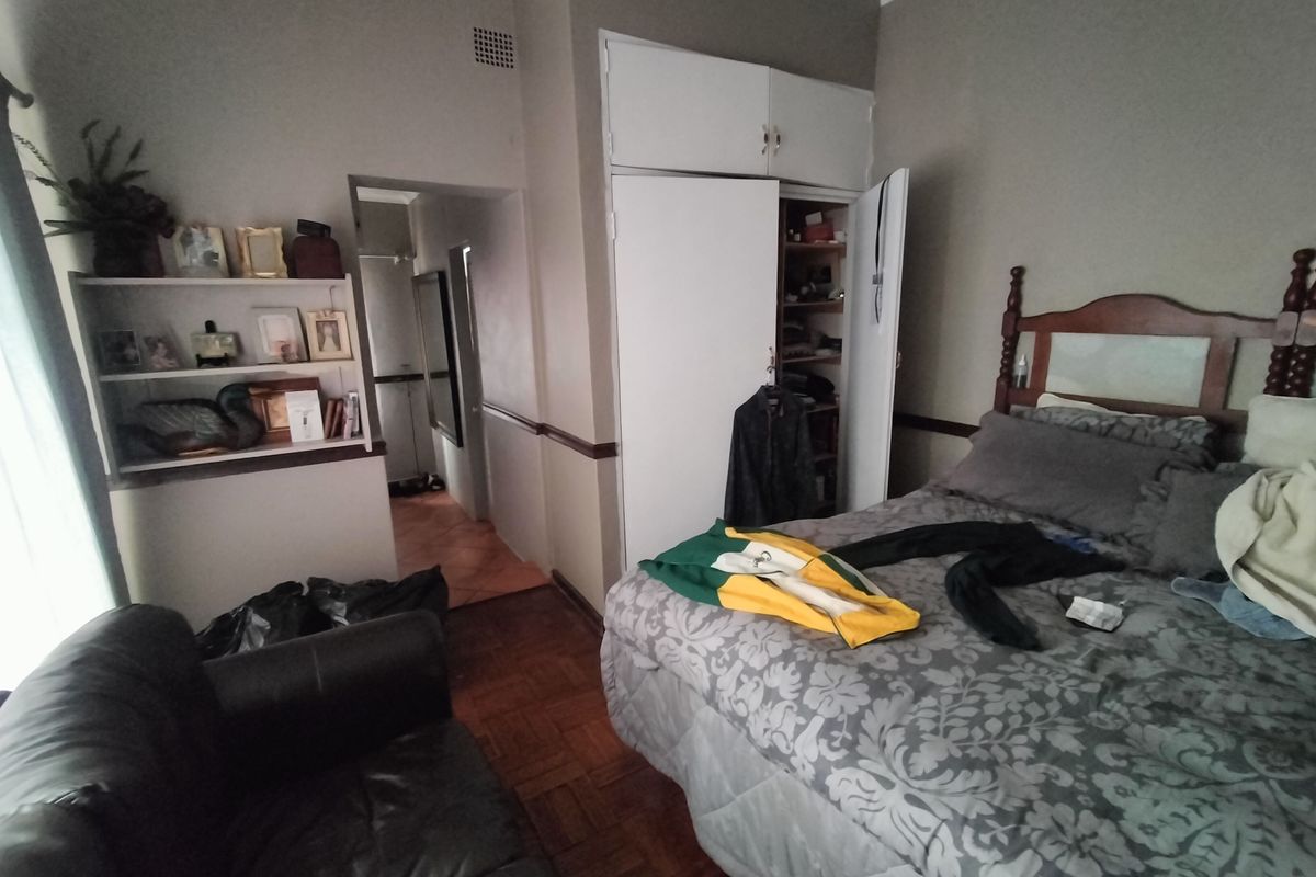 A bedroom featuring parquet flooring, built-in cupboards, and built-in shelving, offering a functional layout with potential for cosmetic updates.