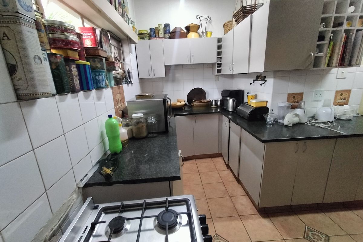 A functional kitchen featuring granite countertops, tiled backsplash, gas hob, and ample built-in cabinetry with ceramic floor tiles.