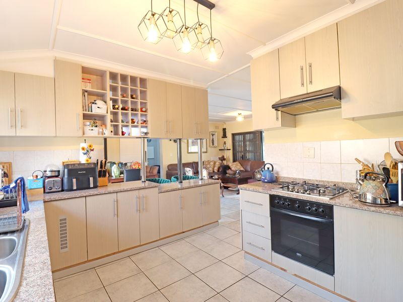 A functional kitchen featuring light wood-finish cabinetry, granite-look laminate countertops, a gas hob with extractor fan, and tiled flooring, opening into the living area.