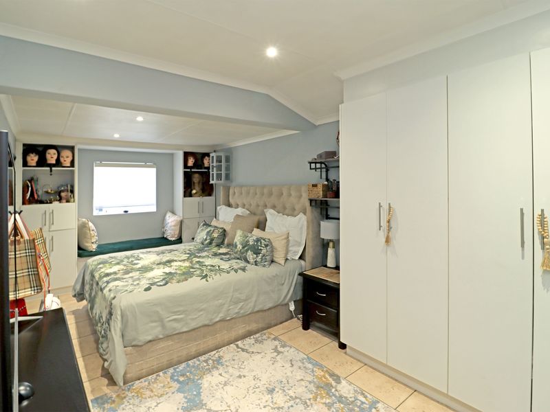 A well-lit bedroom featuring built-in cupboards, a cozy window seat, and tiled flooring, offering a functional and comfortable living space.