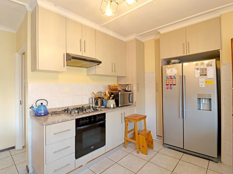 A functional kitchen featuring light wood-finish cabinetry, granite countertops, a gas hob with extractor fan, and tiled flooring.